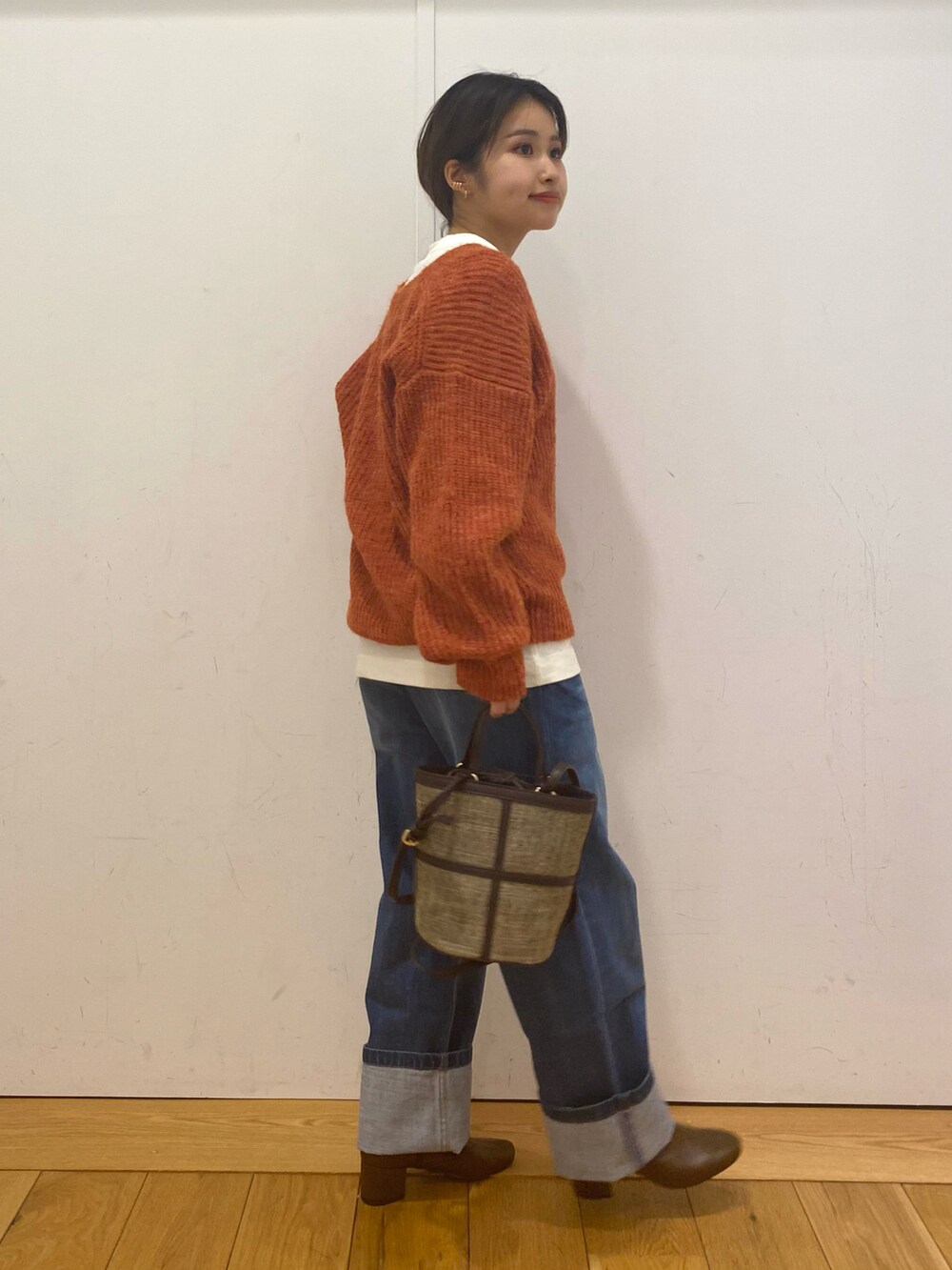 ブルー系のデニムパンツ、オレンジ系のニット/セーター、ブラウン系のショルダーバッグを着用したレディースの冬コーディネートの3枚目の写真