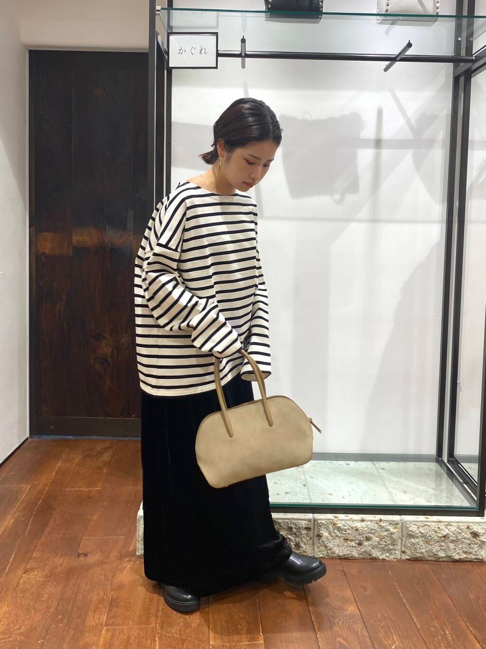 ベージュ系のハンドバッグ、ブラック系のブーツ、ブラック系のスカートを着用したレディースの秋コーディネートの2枚目の写真