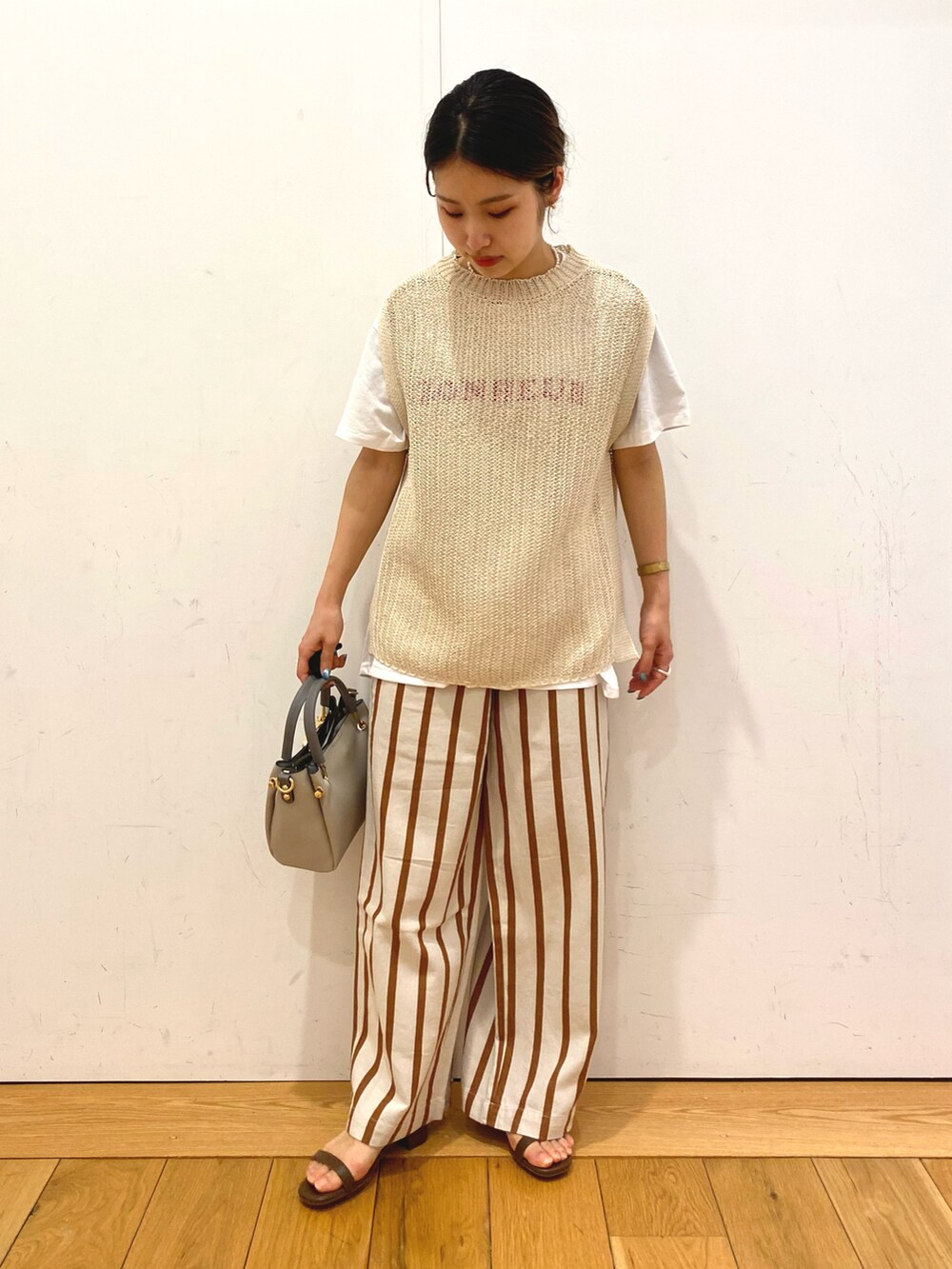グレー系のトートバッグ、ベージュ系のベスト、ホワイト系のその他パンツを着用したレディースの春コーディネートの3枚目の写真