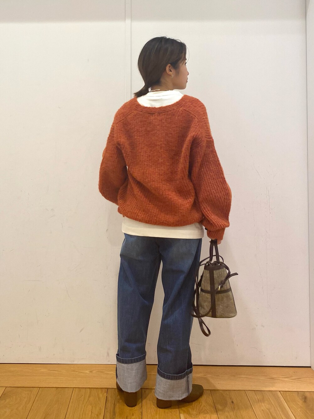 ブルー系のデニムパンツ、オレンジ系のニット/セーター、ブラウン系のショルダーバッグを着用したレディースの冬コーディネートの2枚目の写真