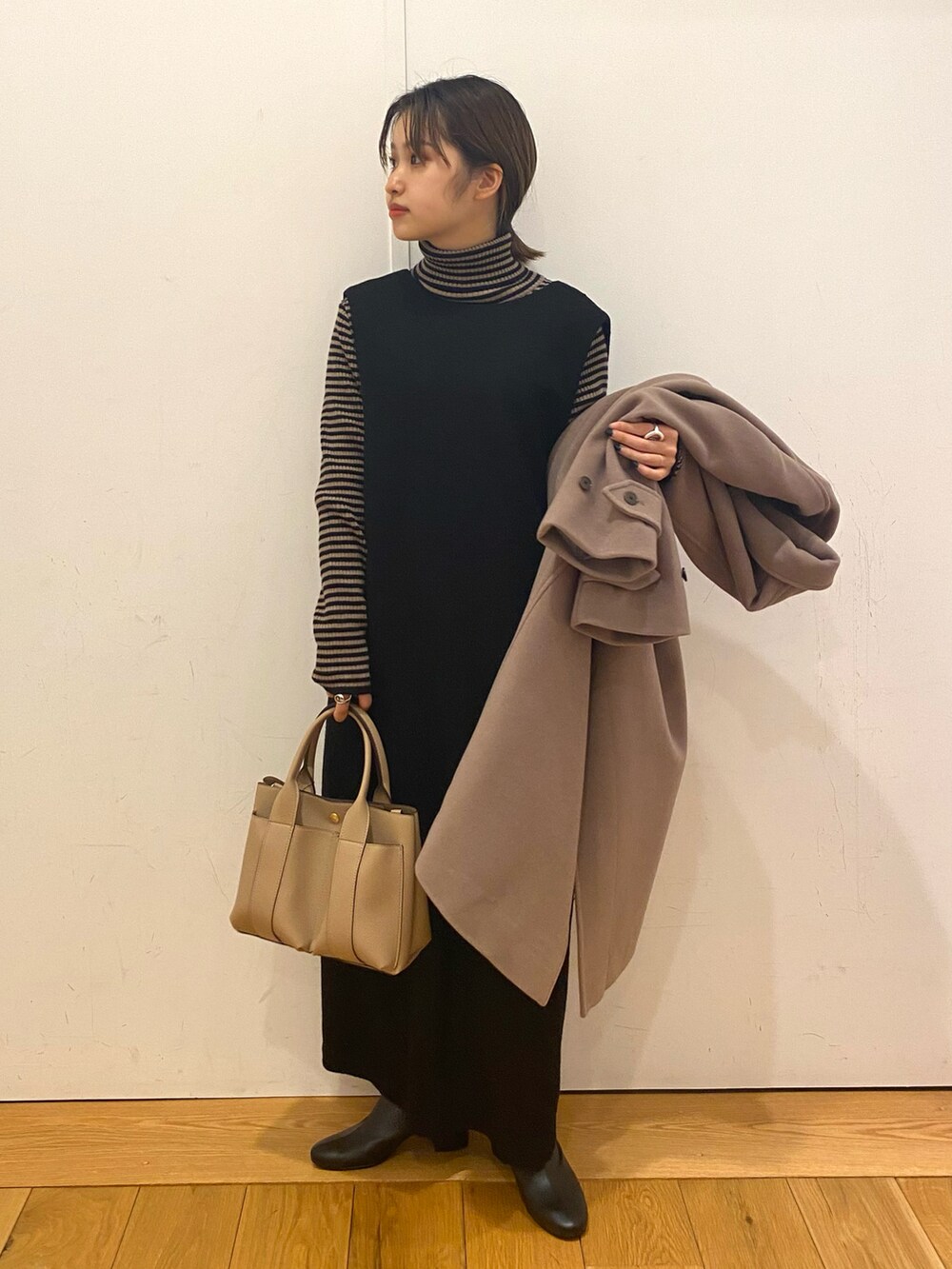 ベージュ系のトートバッグ、ベージュ系のステンカラーコート、ブラック系のワンピースを着用したレディースの冬コーディネートの2枚目の写真