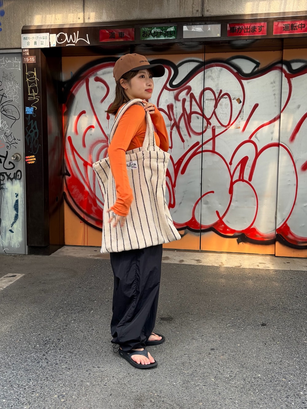 ブラック系のその他パンツ、オレンジ系のTシャツ/カットソー、ホワイト系のトートバッグを着用したレディースの夏コーディネートの2枚目の写真