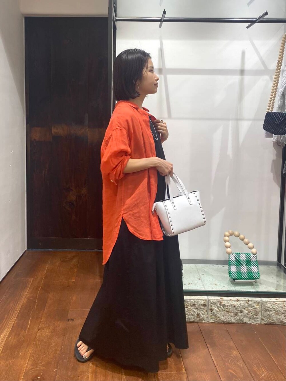 ホワイト系のショルダーバッグ、オレンジ系のTシャツ/カットソー、ブラック系のワンピースを着用したレディースの夏コーディネートの2枚目の写真