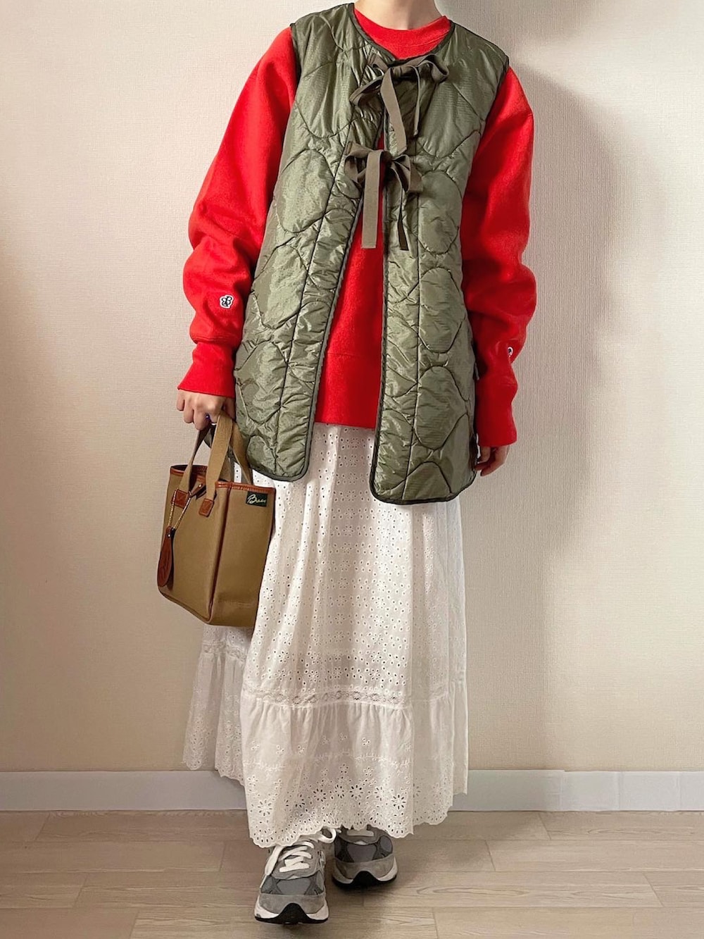 ホワイト系のスカート、グリーン系のベスト、オレンジ系のスウェットを着用したレディースの秋コーディネートの2枚目の写真