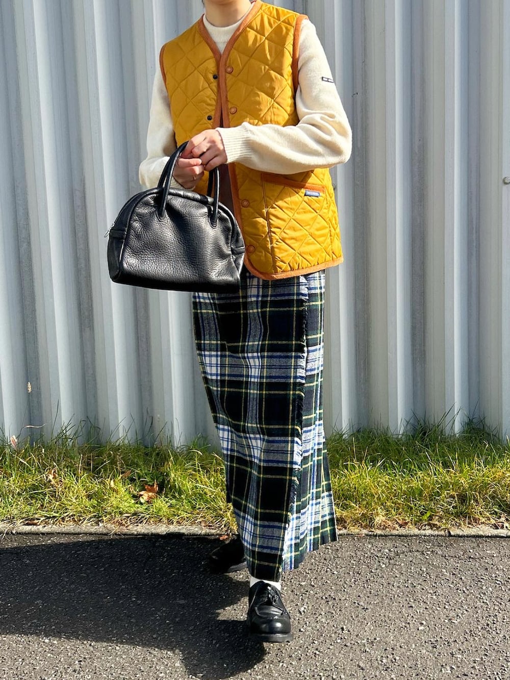 イエロー系のダウンベスト、ブラック系のボストンバッグ、グリーン系のスカートを着用したレディースの秋コーディネートの4枚目の写真