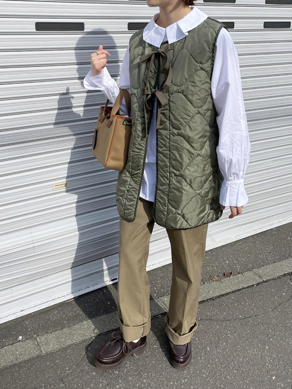 グリーン系のベスト、ブラウン系のハンドバッグ、ベージュ系のチノパンツを着用したレディースの秋コーディネートの2枚目の写真