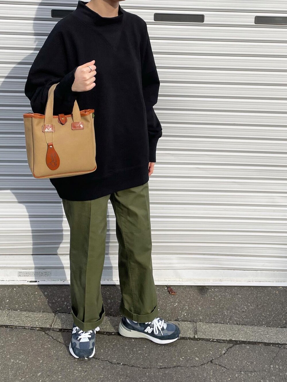 ブラック系のスウェット、ブラウン系のハンドバッグ、ブルー系のスニーカーを着用したレディースの秋コーディネートの3枚目の写真