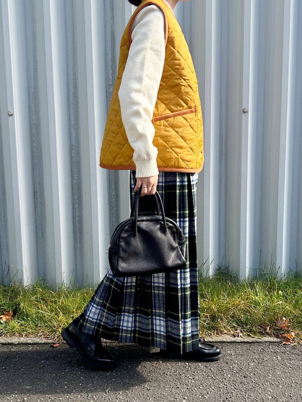 イエロー系のダウンベスト、ブラック系のボストンバッグ、グリーン系のスカートを着用したレディースの秋コーディネートの3枚目の写真