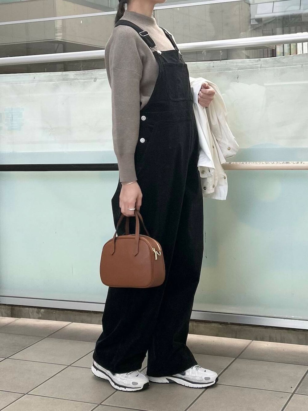 ブラウン系のショルダーバッグ、ベージュ系のニット/セーター、ブラック系のサロペット/オーバーオールを着用したレディースの冬コーディネートの4枚目の写真