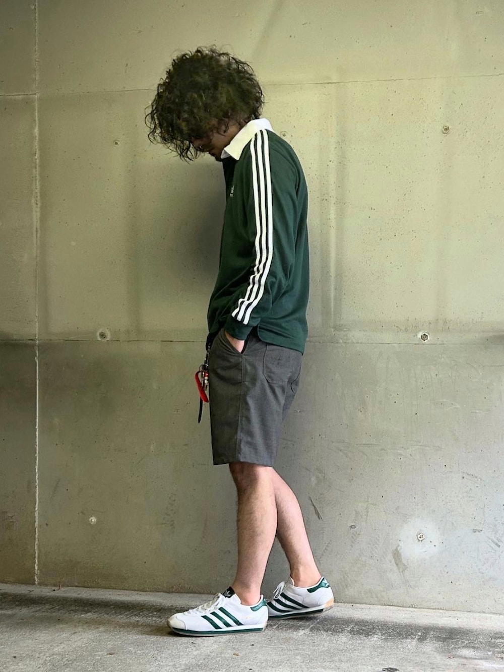 ホワイト系のスニーカー、グリーン系のポロシャツ、グレー系のパンツを着用したメンズの秋コーディネートの2枚目の写真