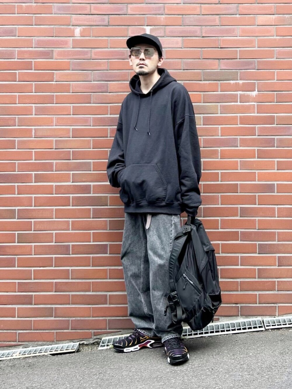 ベージュ系のステンカラーコート、ブラック系のパーカー、ブラック系のデニムパンツを着用したメンズの春コーディネートの2枚目の写真