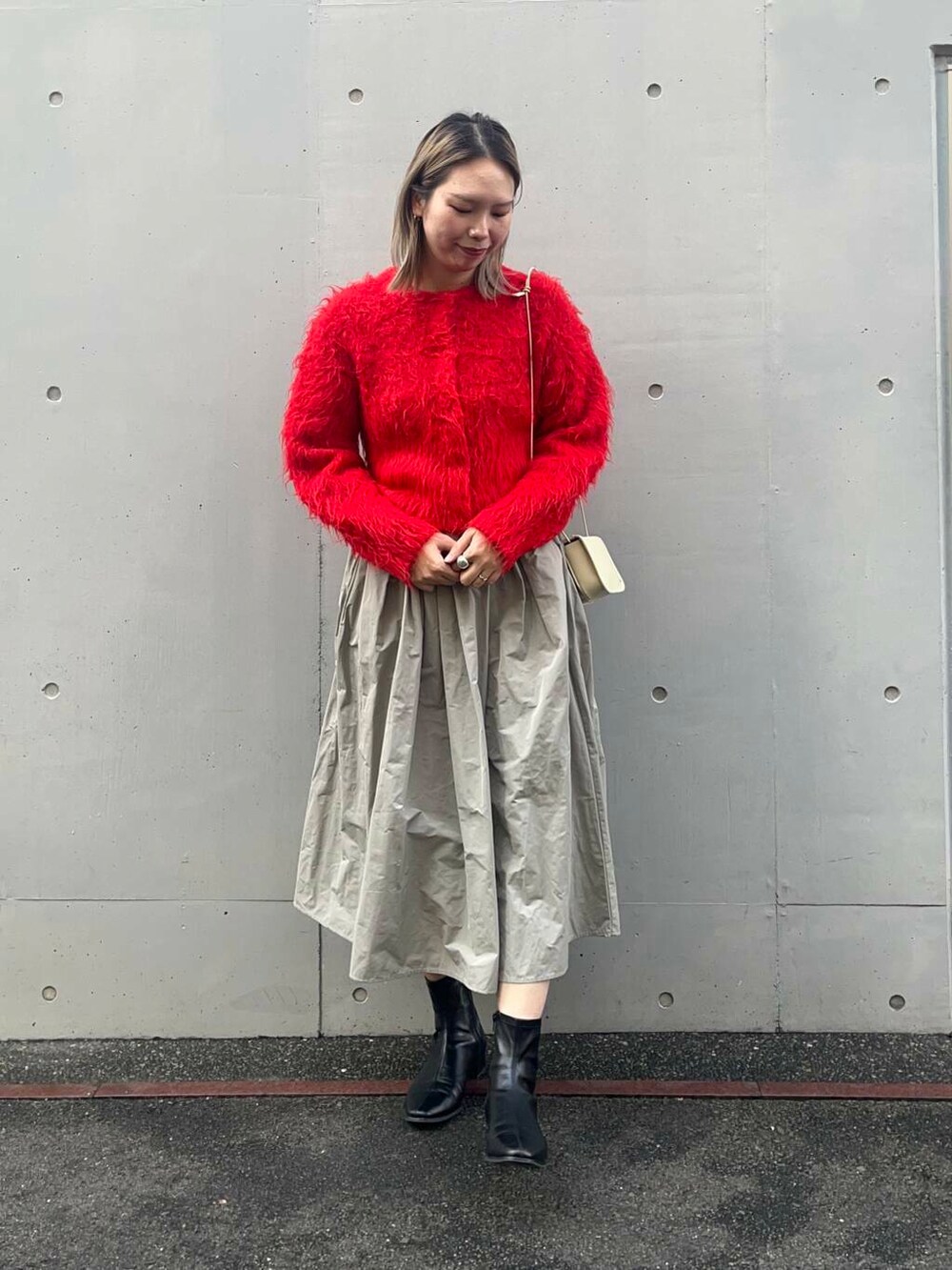 レッド系のカーディガン/ボレロ、ホワイト系のショルダーバッグ、グリーン系のスカートを着用したレディースの冬コーディネートの2枚目の写真