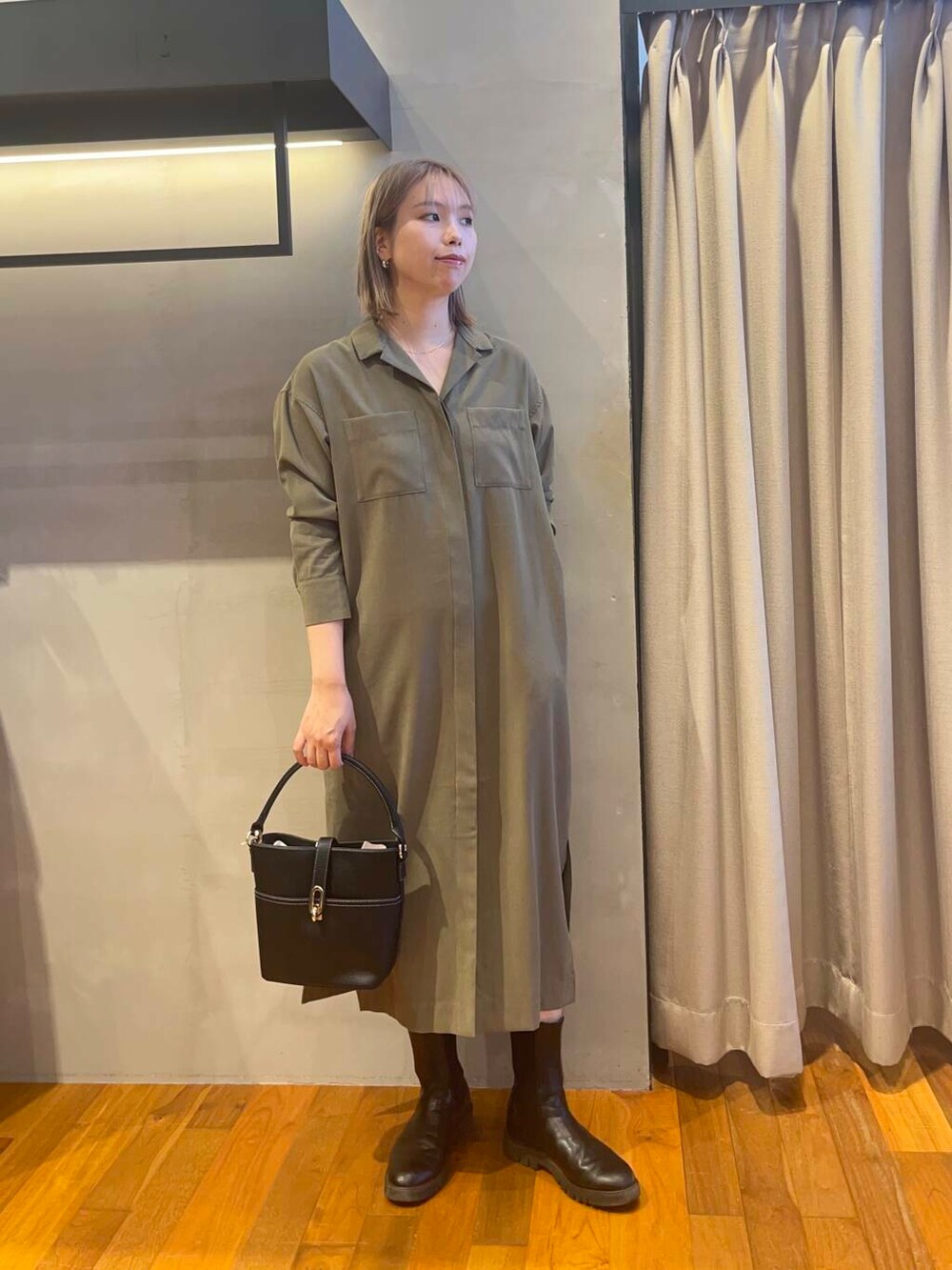 ブラック系のハンドバッグ、グリーン系のワンピース、ゴールド系のネックレスを着用したレディースの秋コーディネートの2枚目の写真