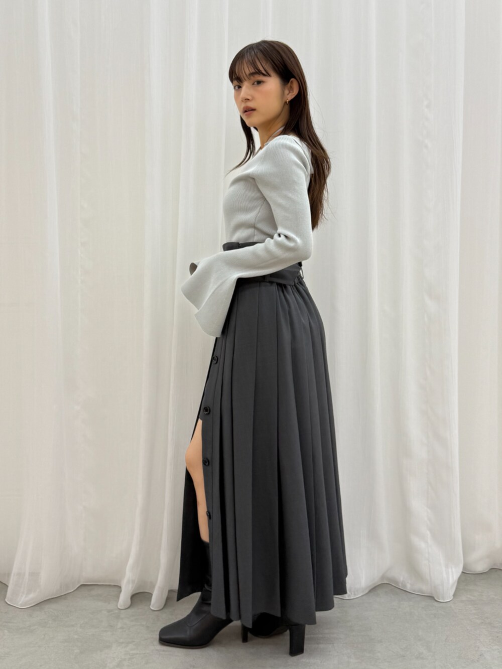 グレー系のスカート、グレー系のニット/セーター、ブラック系のブーツを着用したレディースの秋コーディネートの2枚目の写真