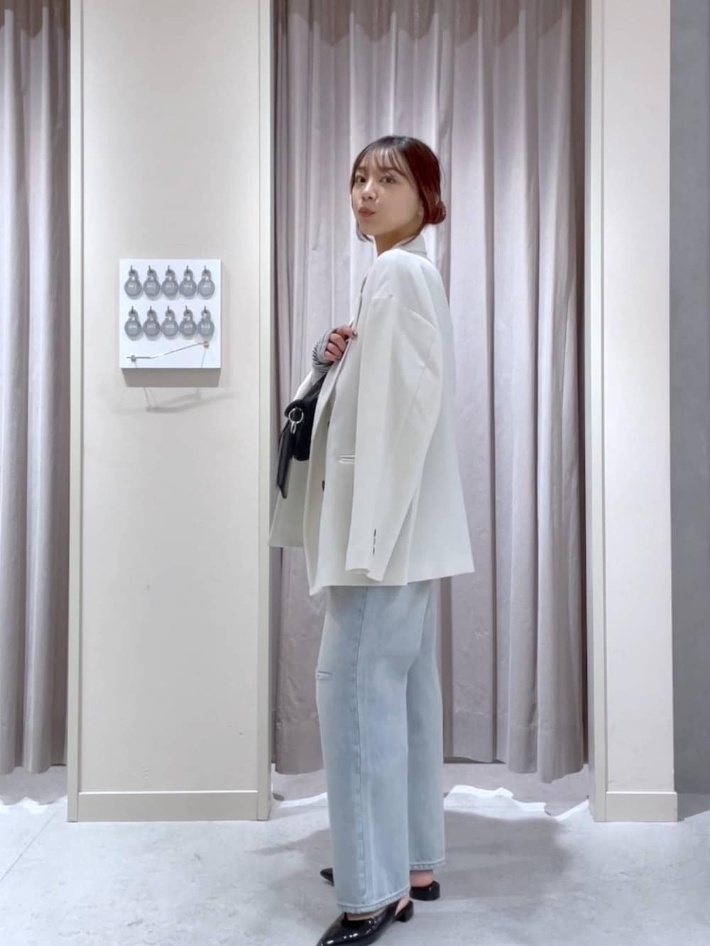 ホワイト系のテーラードジャケット、ブルー系のデニムパンツ、ブラック系のショルダーバッグを着用したレディースの春コーディネートの2枚目の写真