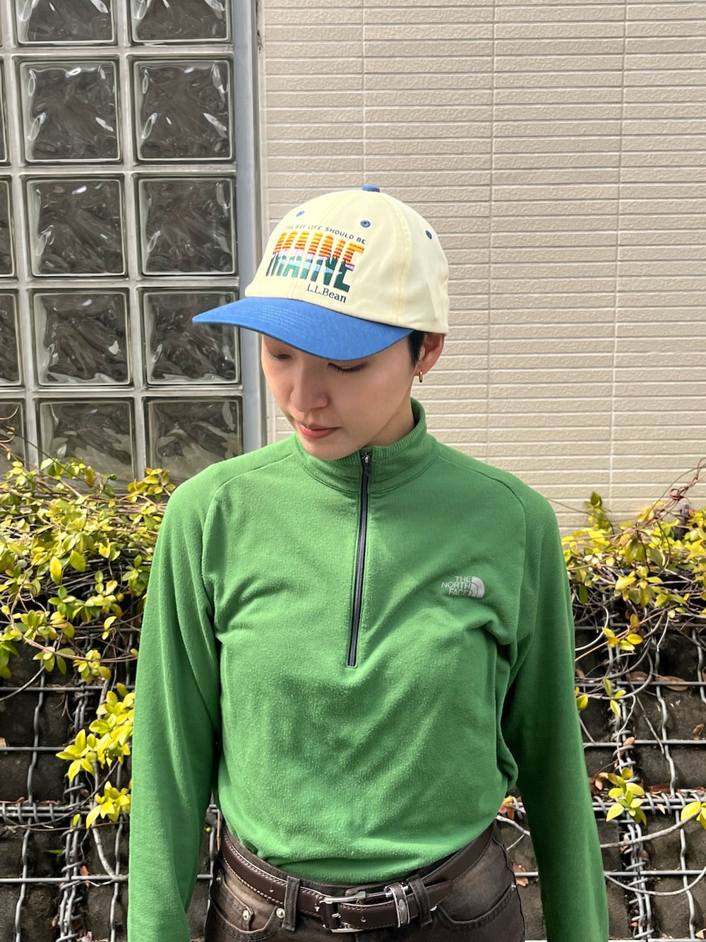 グリーン系のトップス、ブラウン系のデニムパンツ、ブラック系のスニーカーを着用したレディースの春コーディネートの2枚目の写真