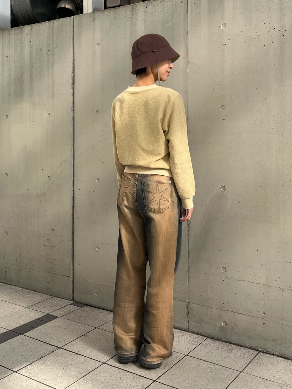 イエロー系のトップス、ブラウン系のデニムパンツ、ブラック系のスニーカーを着用したレディースの秋コーディネートの2枚目の写真
