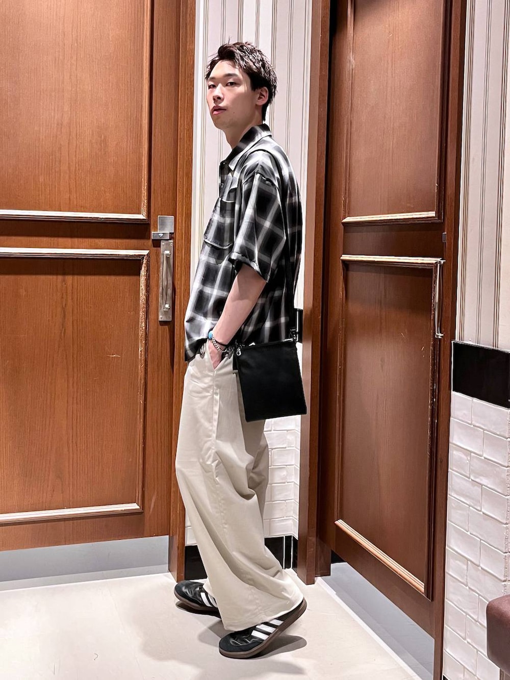 ホワイト系のスラックス、ブラック系のショルダーバッグ、ブラック系のシャツ/ブラウスを着用したメンズの夏コーディネートの3枚目の写真