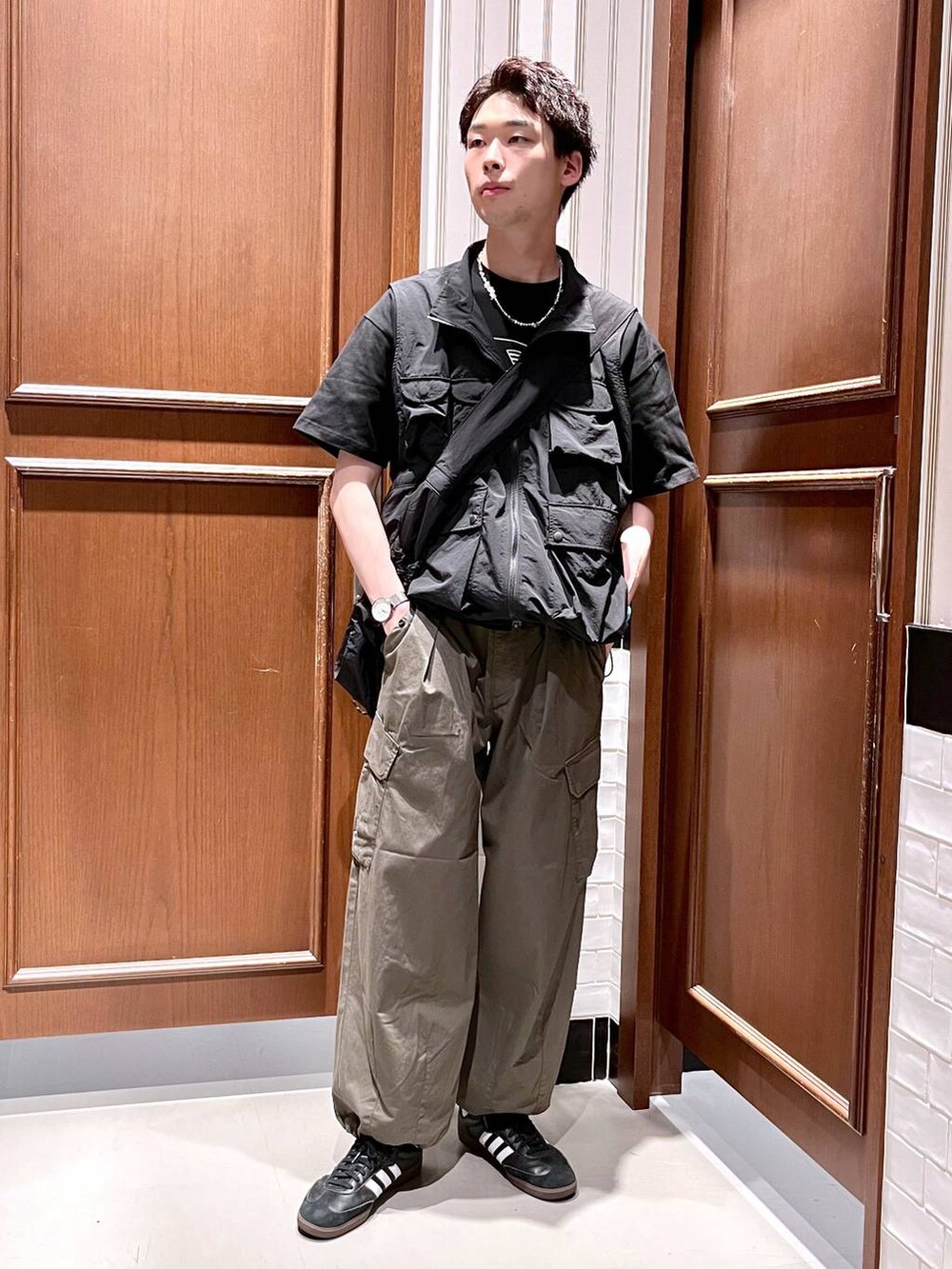 グリーン系のカーゴパンツ、ブラック系のショルダーバッグ、ブラック系のベストを着用したメンズの夏コーディネートの2枚目の写真
