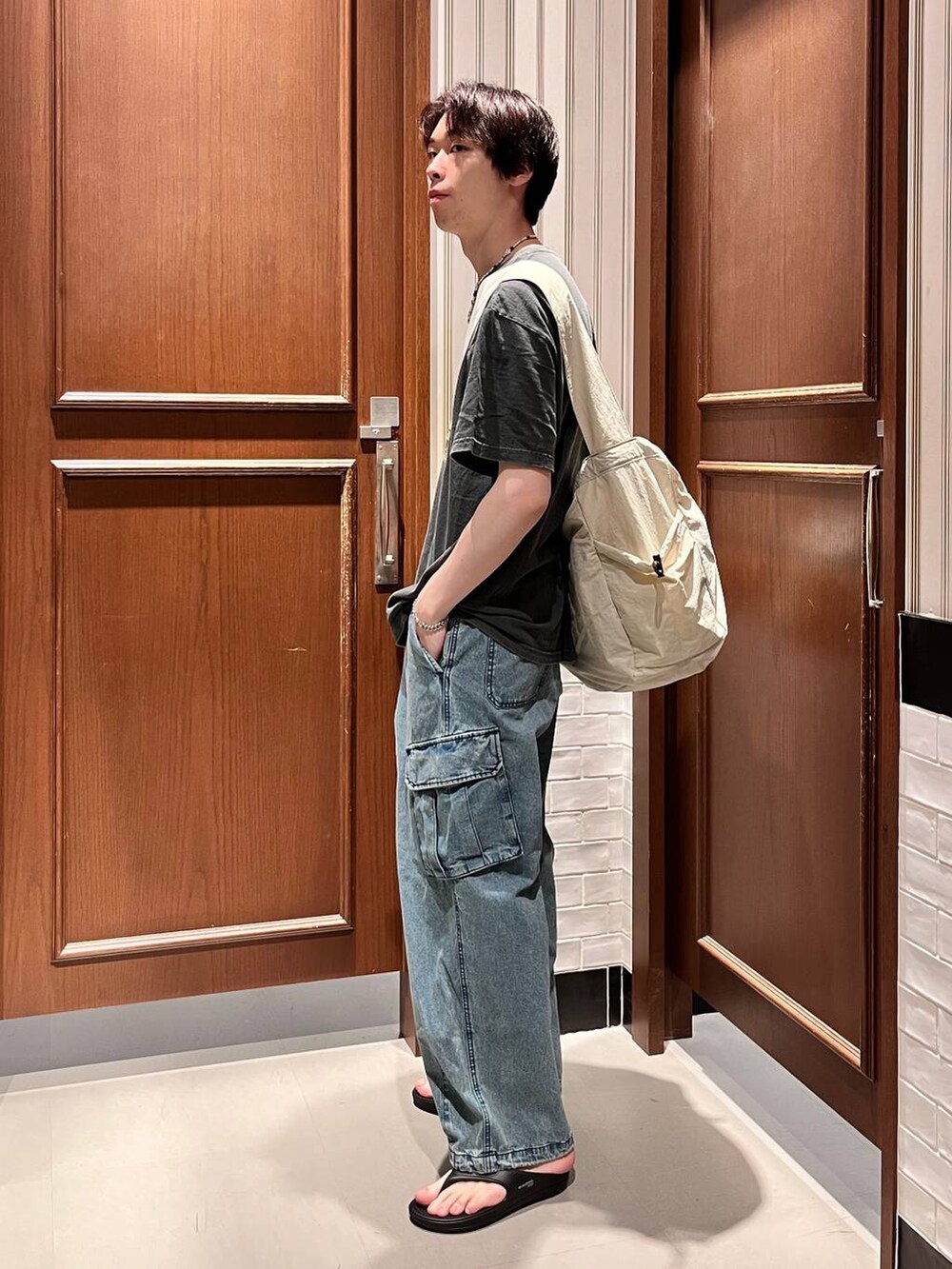 ブラック系のサンダル、ブルー系のデニムパンツ、ホワイト系のショルダーバッグを着用したメンズの夏コーディネートの3枚目の写真