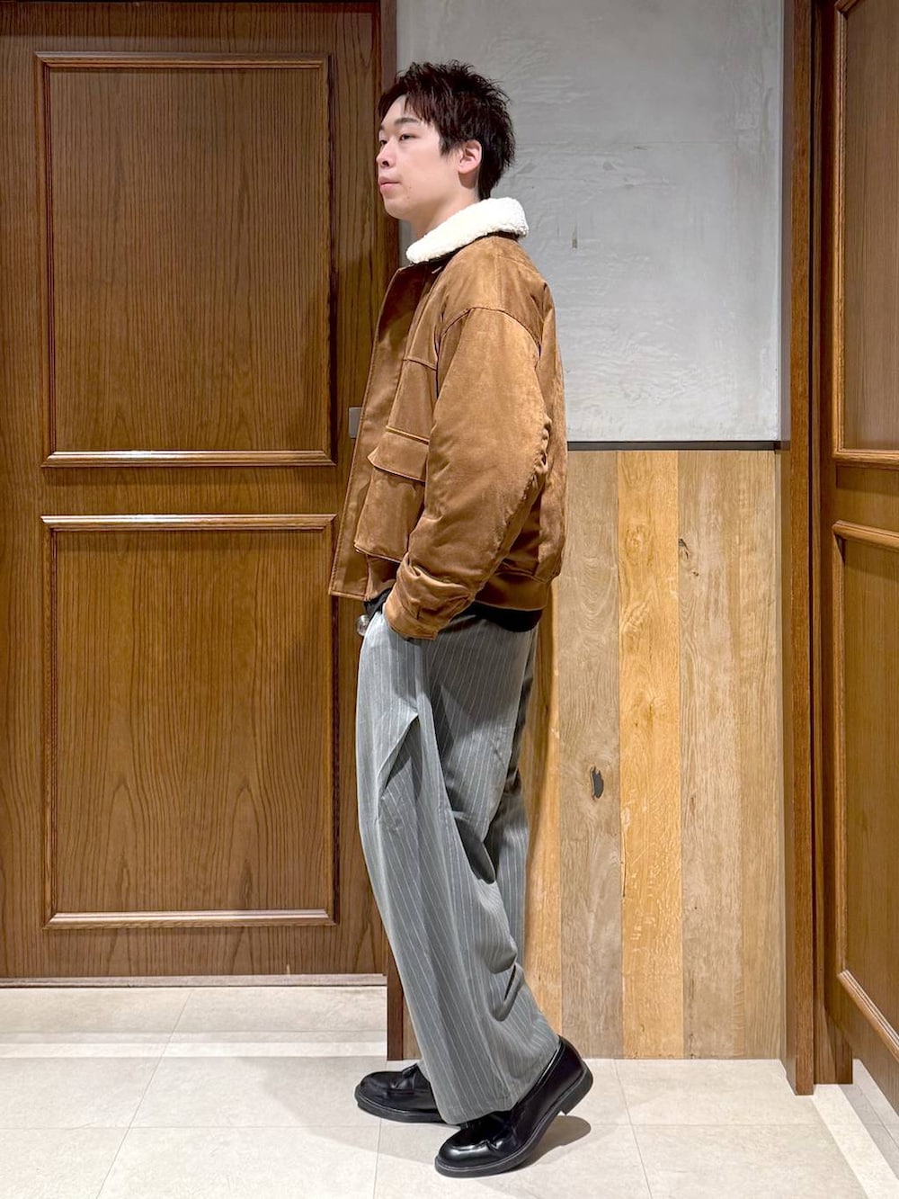 イエロー系のブルゾン、ブラック系のポロシャツ、グレー系のスラックスを着用したメンズの冬コーディネートの4枚目の写真