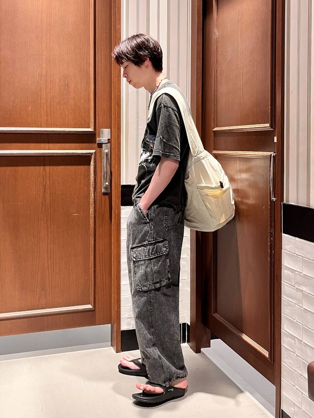 ブラック系のサンダル、グレー系のデニムパンツ、ホワイト系のショルダーバッグを着用したメンズの夏コーディネートの3枚目の写真