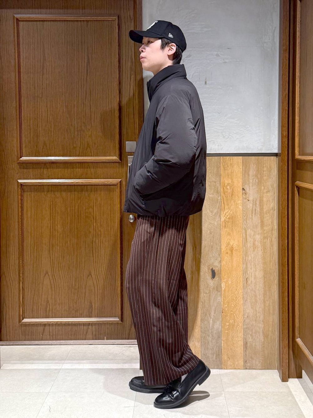 ブラック系のダウンジャケット/コート、グレー系のニット/セーター、ブラウン系のスラックスを着用したメンズの冬コーディネートの6枚目の写真