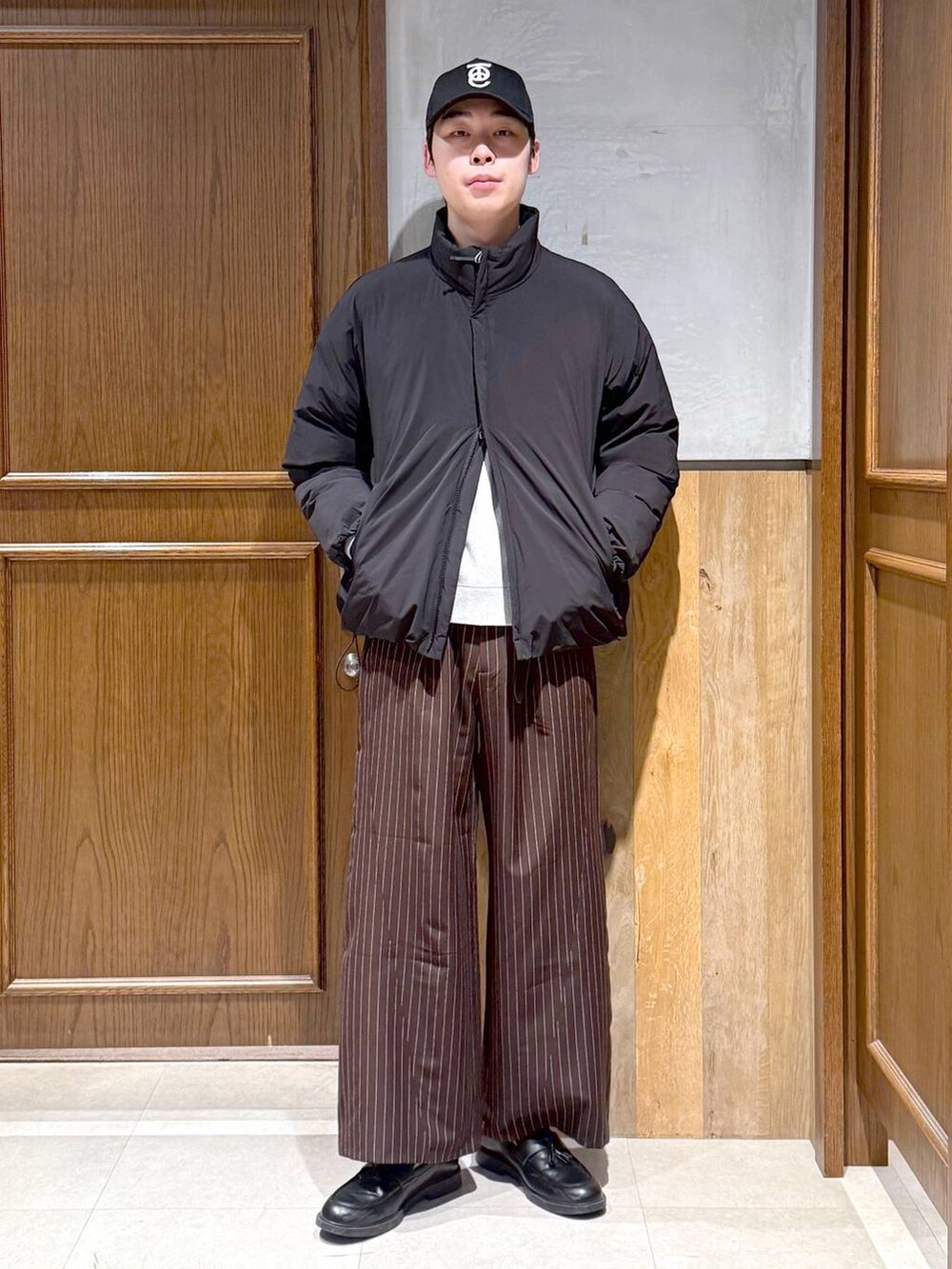 ブラック系のダウンジャケット/コート、グレー系のニット/セーター、ブラウン系のスラックスを着用したメンズの冬コーディネートの3枚目の写真