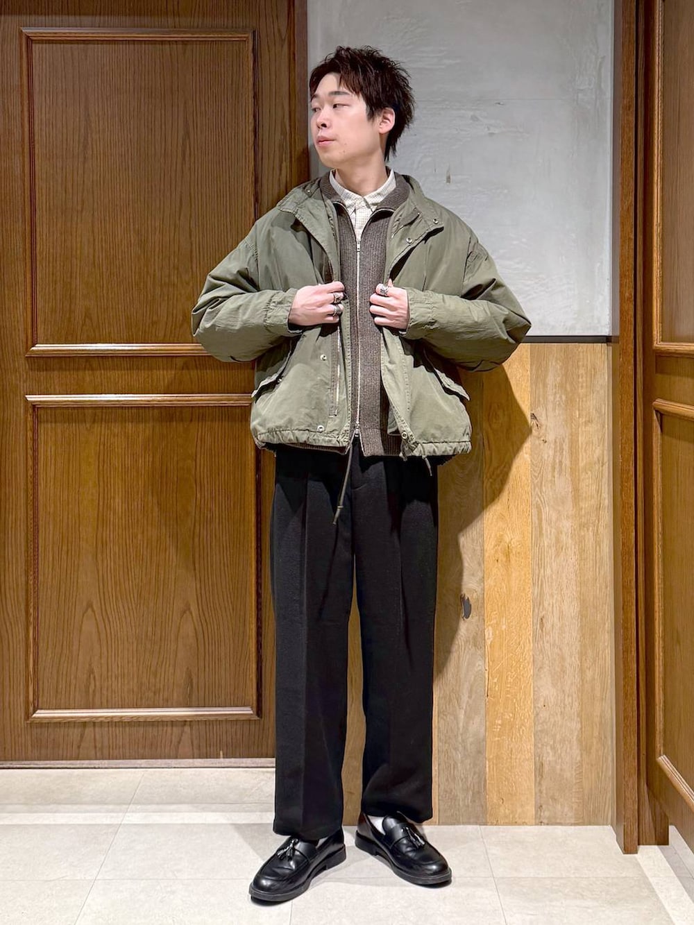 グリーン系のモッズコート、ブラック系のスラックス、ホワイト系のシャツ/ブラウスを着用したメンズの冬コーディネートの2枚目の写真
