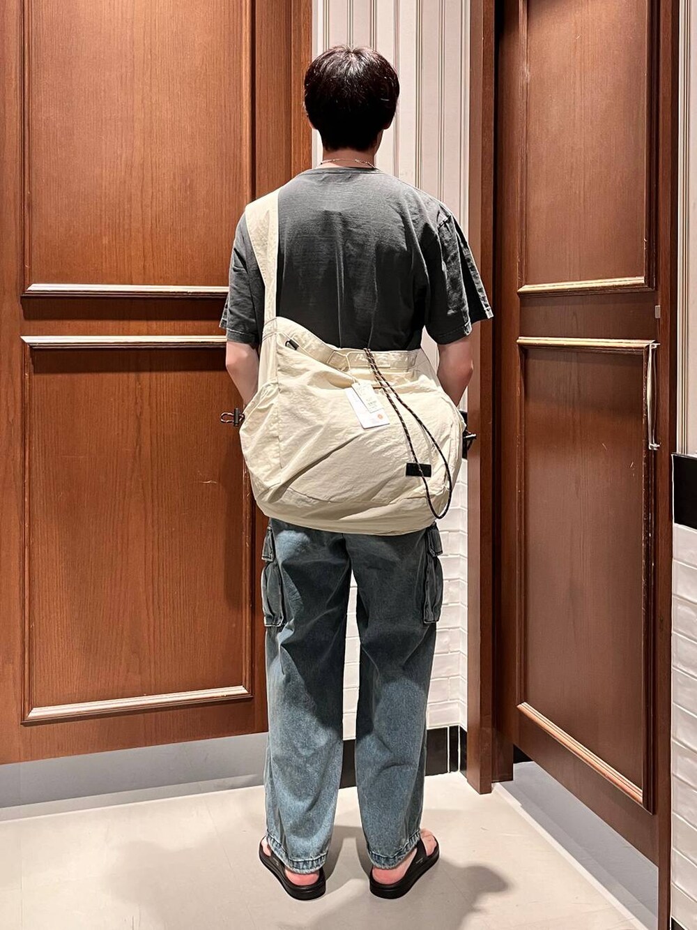 ブラック系のサンダル、ブルー系のデニムパンツ、ホワイト系のショルダーバッグを着用したメンズの夏コーディネートの5枚目の写真