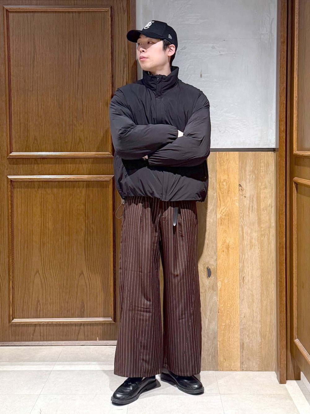 ブラック系のダウンジャケット/コート、グレー系のニット/セーター、ブラウン系のスラックスを着用したメンズの冬コーディネートの2枚目の写真