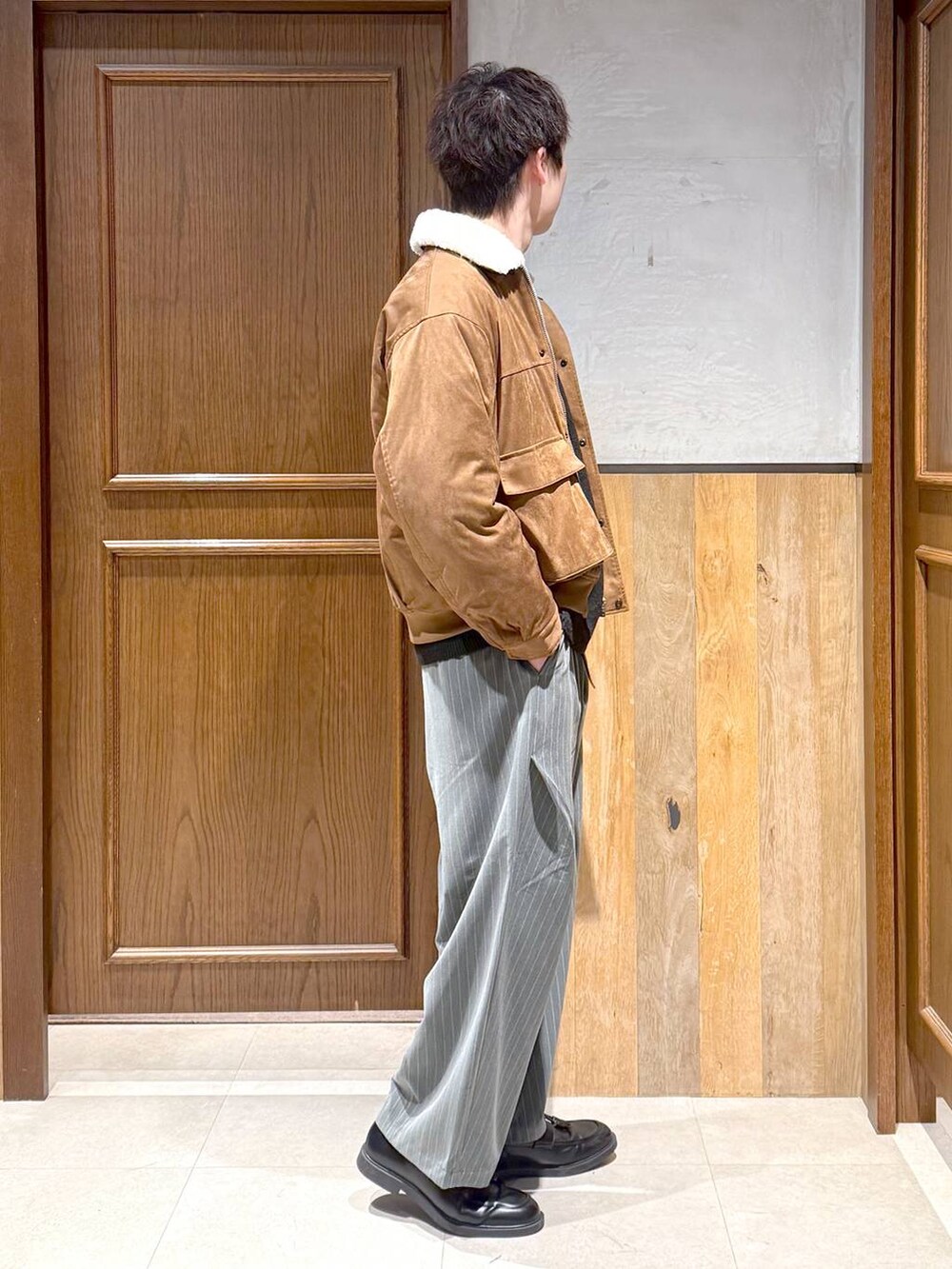 イエロー系のブルゾン、ブラック系のポロシャツ、グレー系のスラックスを着用したメンズの冬コーディネートの6枚目の写真