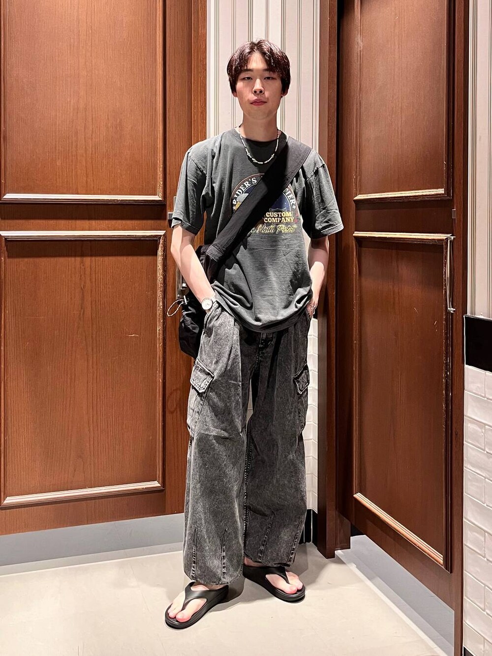 ブラック系のサンダル、グレー系のデニムパンツ、ブラック系のショルダーバッグを着用したメンズの夏コーディネートの2枚目の写真