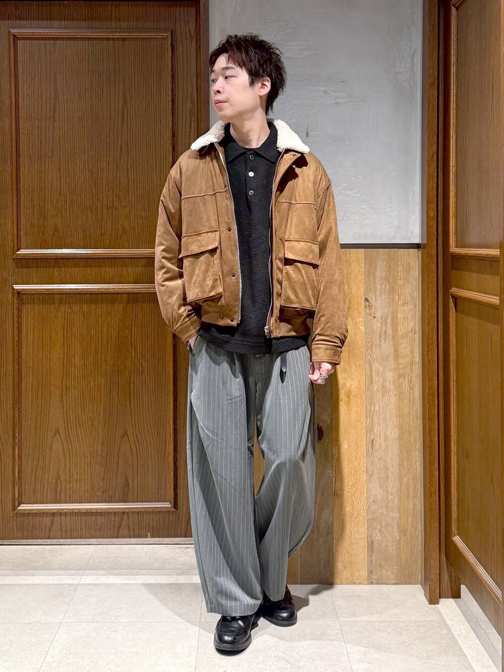 イエロー系のブルゾン、ブラック系のポロシャツ、グレー系のスラックスを着用したメンズの冬コーディネートの8枚目の写真