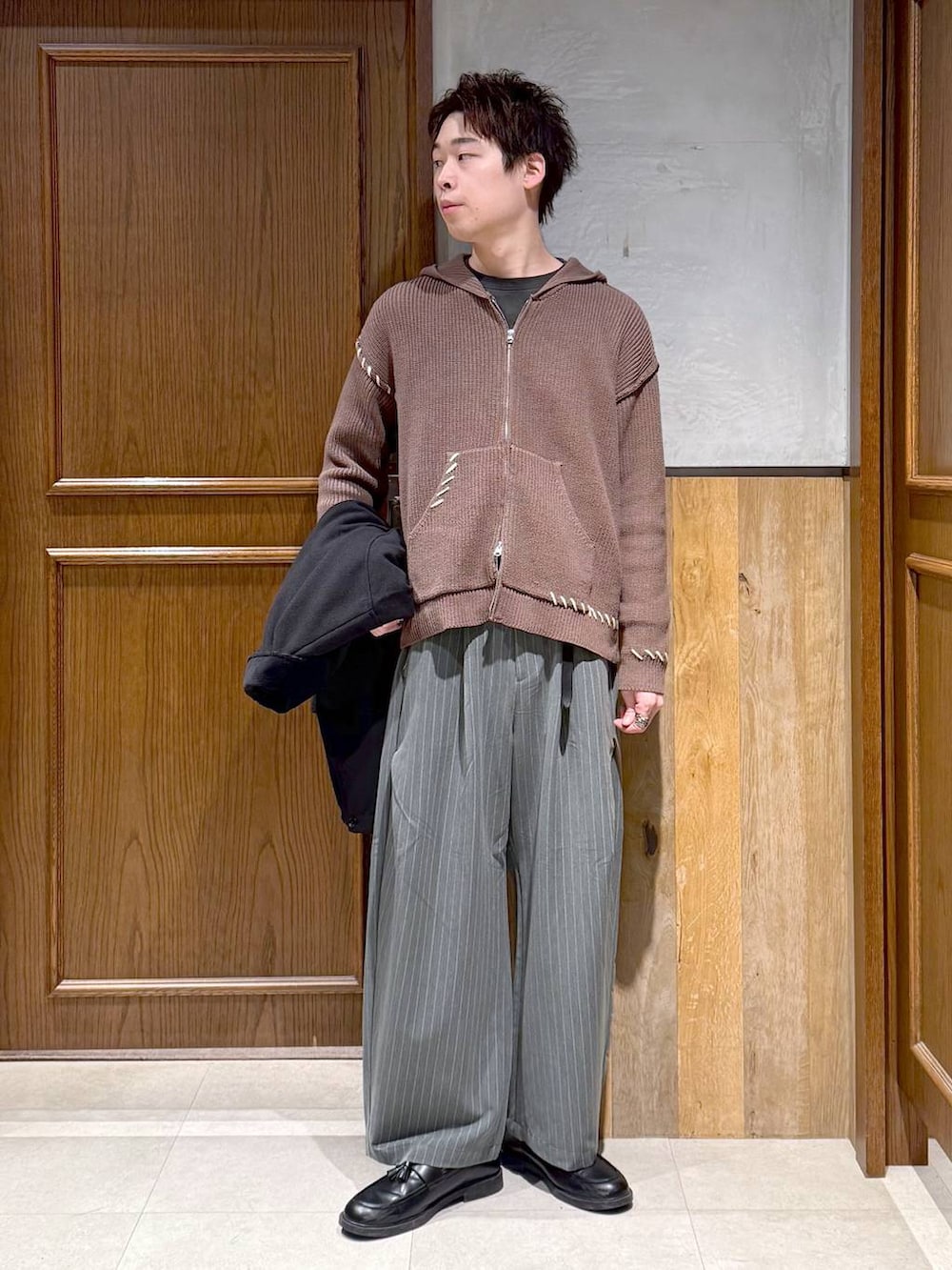 ブラック系のブルゾン、ブラウン系のニット/セーター、グレー系のスラックスを着用したメンズの冬コーディネートの2枚目の写真