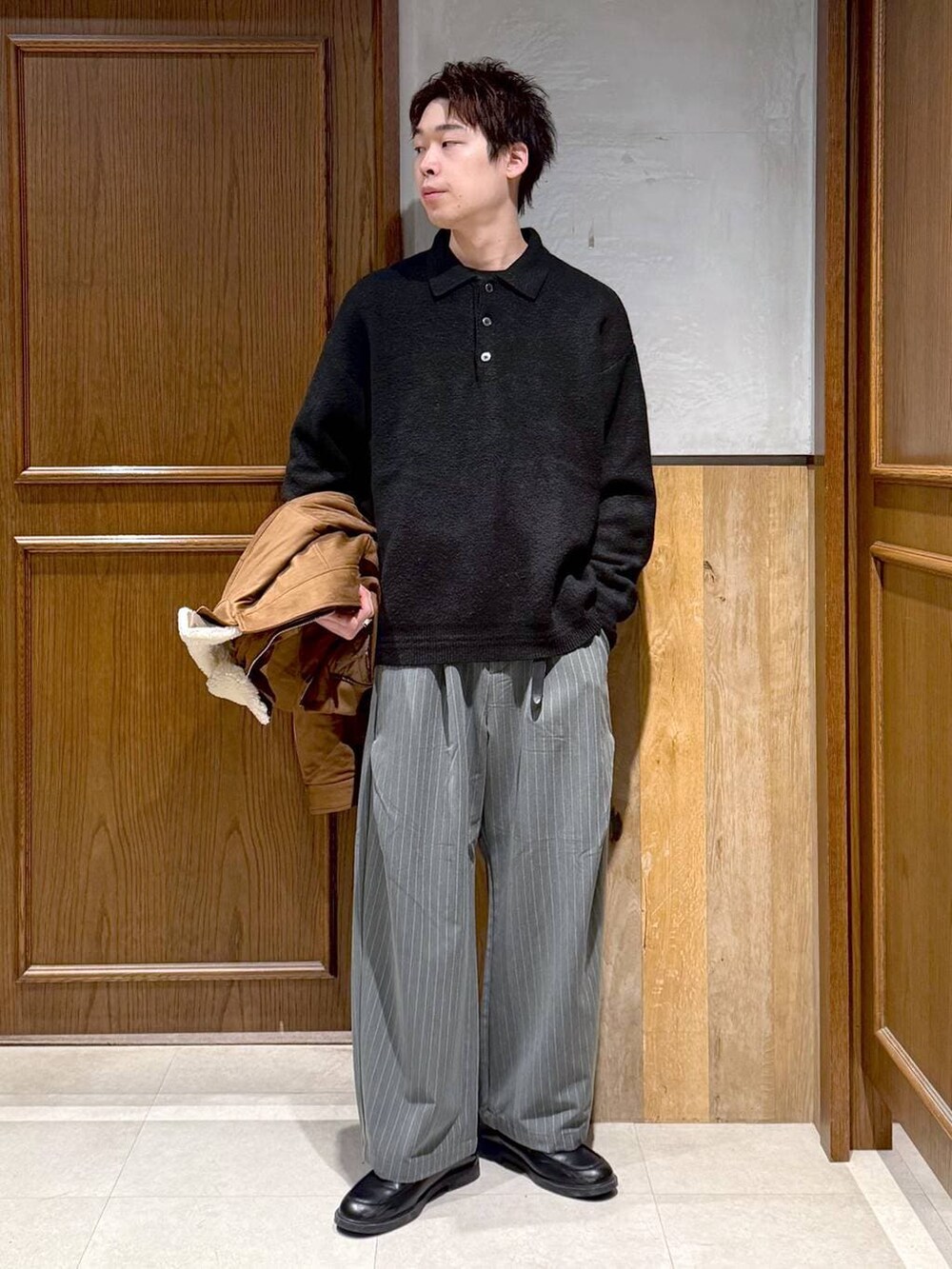 イエロー系のブルゾン、ブラック系のポロシャツ、グレー系のスラックスを着用したメンズの冬コーディネートの2枚目の写真