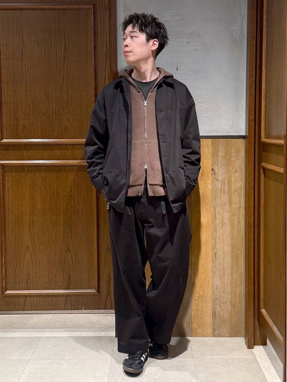 ブラック系のチノパンツ、ブラック系のステンカラーコート、ブラウン系のニット/セーターを着用したメンズの冬コーディネートの2枚目の写真