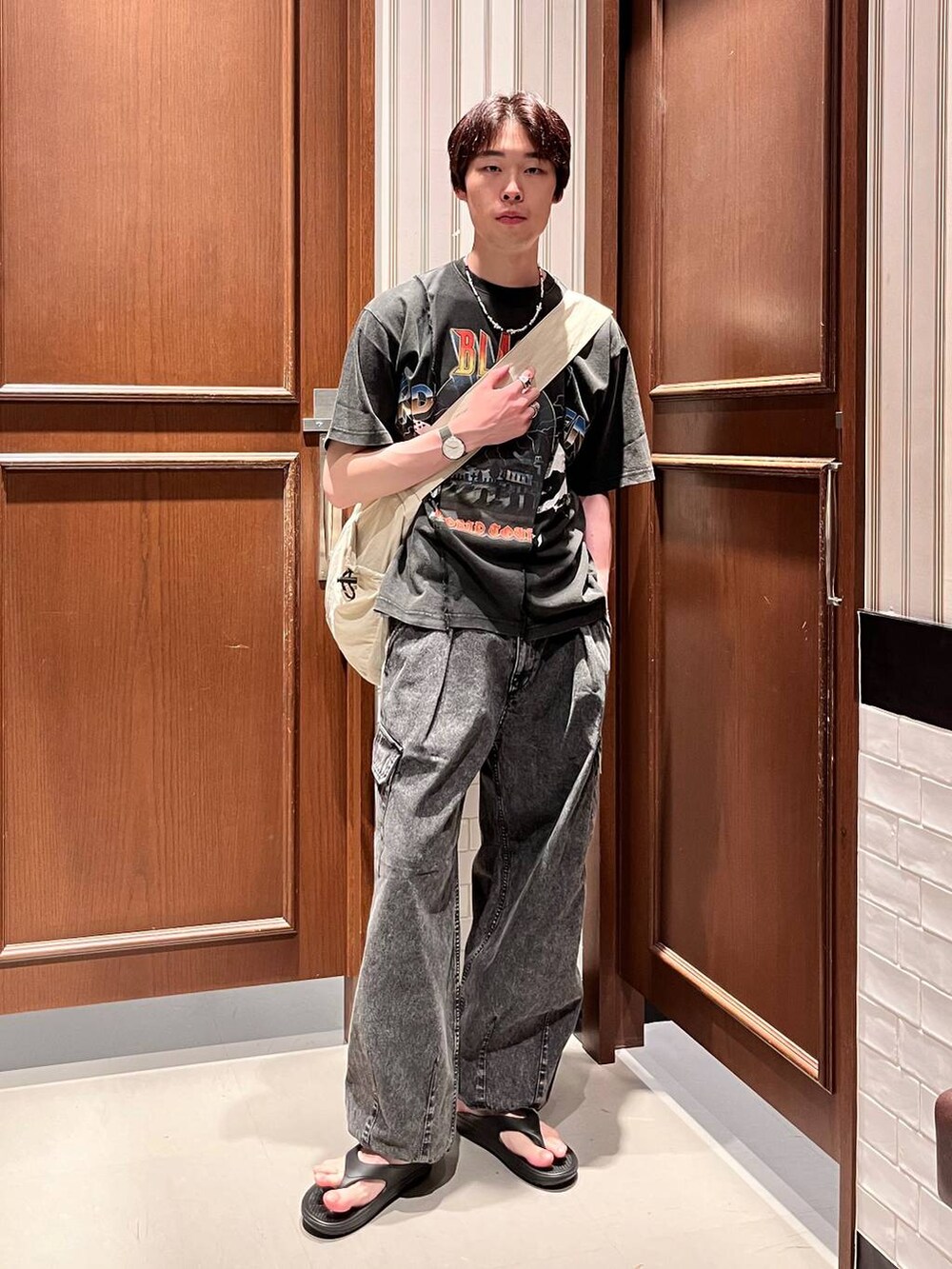 ブラック系のサンダル、グレー系のデニムパンツ、ホワイト系のショルダーバッグを着用したメンズの夏コーディネートの2枚目の写真