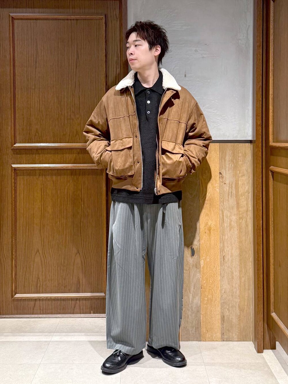 イエロー系のブルゾン、ブラック系のポロシャツ、グレー系のスラックスを着用したメンズの冬コーディネートの7枚目の写真