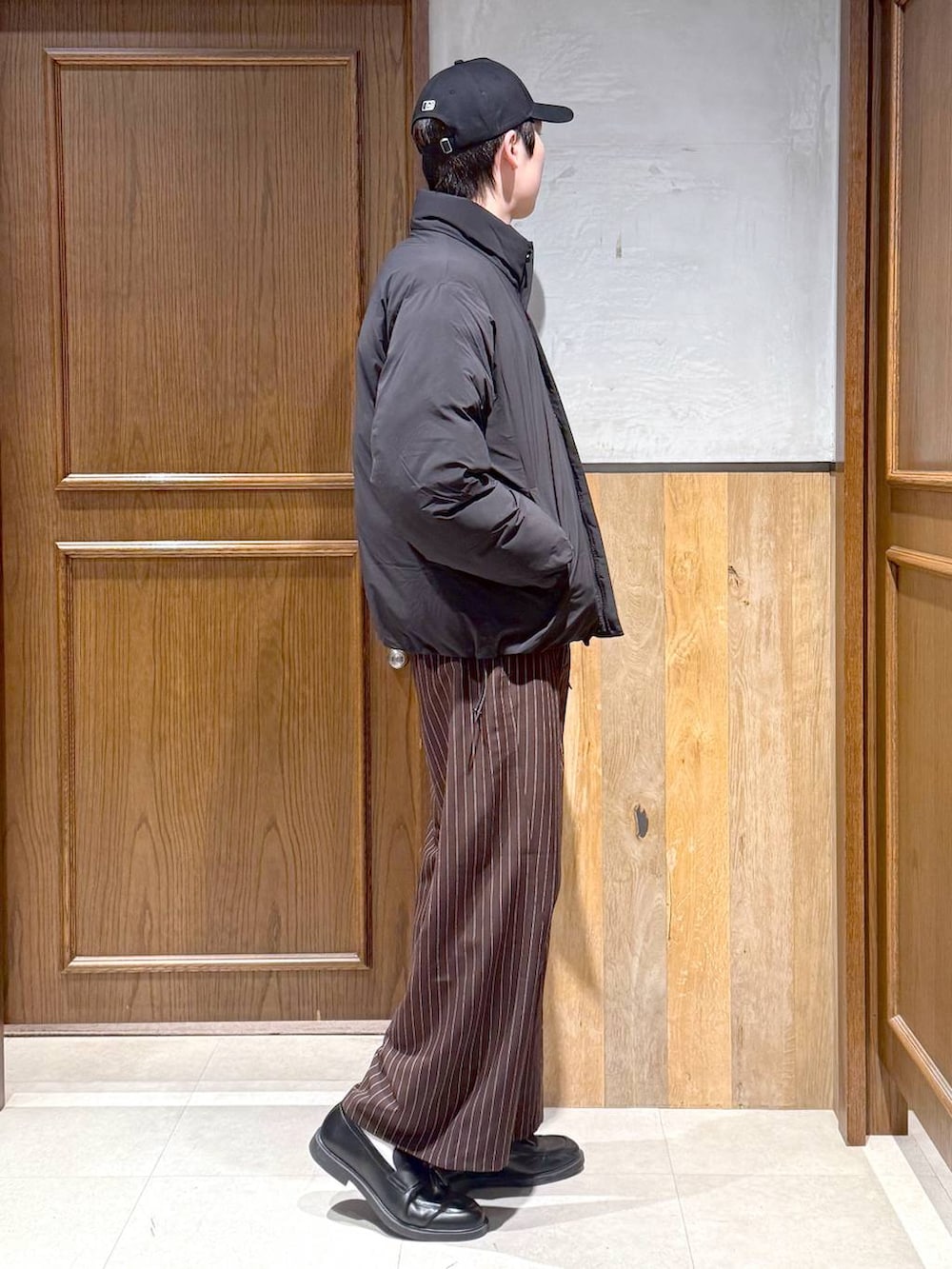 ブラック系のダウンジャケット/コート、グレー系のニット/セーター、ブラウン系のスラックスを着用したメンズの冬コーディネートの4枚目の写真