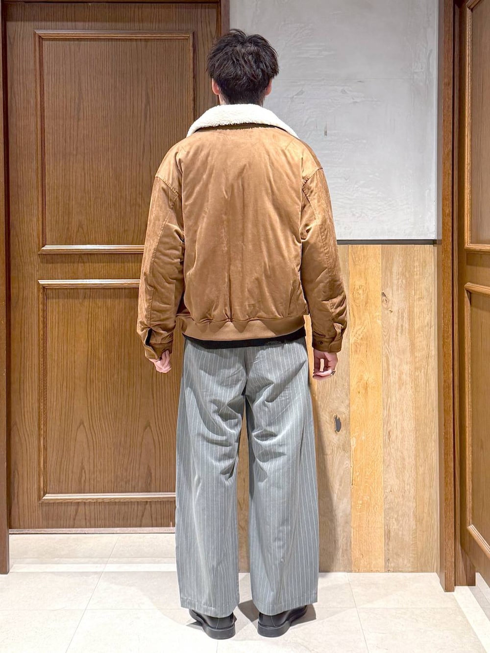 イエロー系のブルゾン、ブラック系のポロシャツ、グレー系のスラックスを着用したメンズの冬コーディネートの5枚目の写真