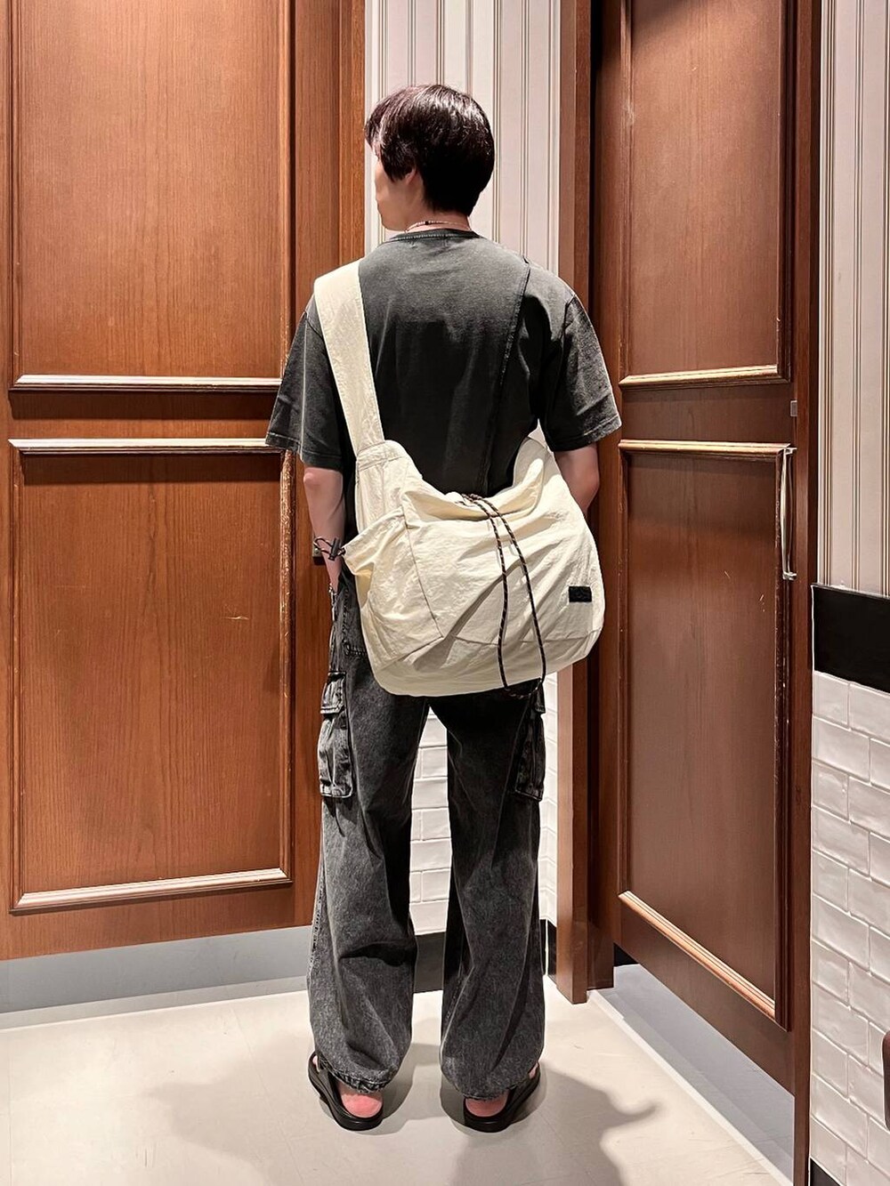 ブラック系のサンダル、グレー系のデニムパンツ、ホワイト系のショルダーバッグを着用したメンズの夏コーディネートの5枚目の写真