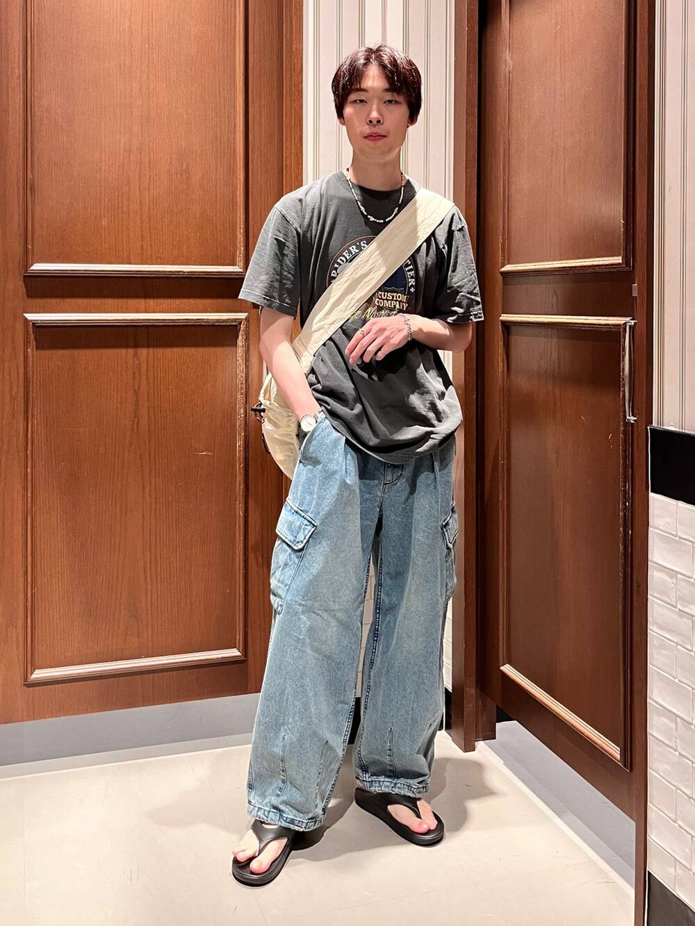 ブラック系のサンダル、ブルー系のデニムパンツ、ホワイト系のショルダーバッグを着用したメンズの夏コーディネートの2枚目の写真