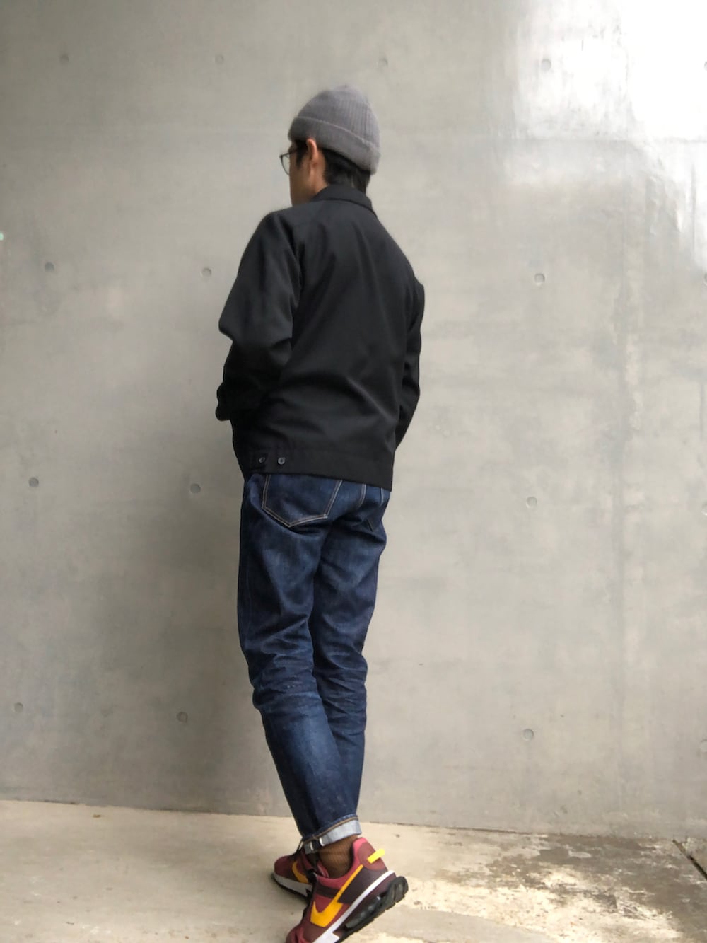 ブラック系のブルゾン、ブルー系のデニムパンツ、レッド系のスニーカーを着用したメンズの秋コーディネートの2枚目の写真