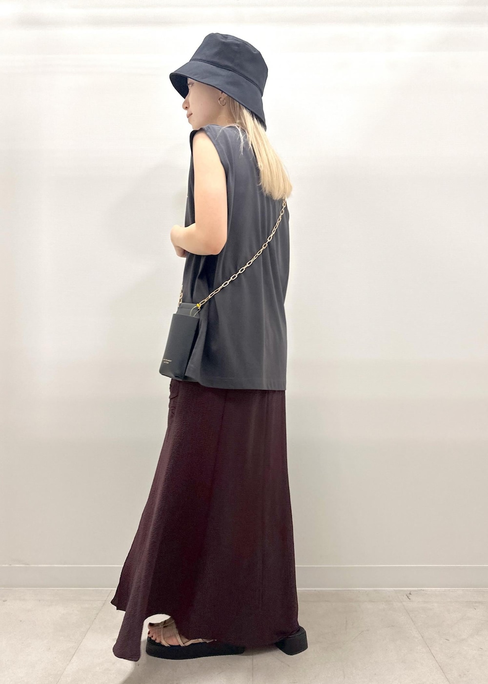 ブラック系のショルダーバッグ、ゴールド系のサンダル、グレー系のTシャツ/カットソーを着用したレディースの夏コーディネートの4枚目の写真