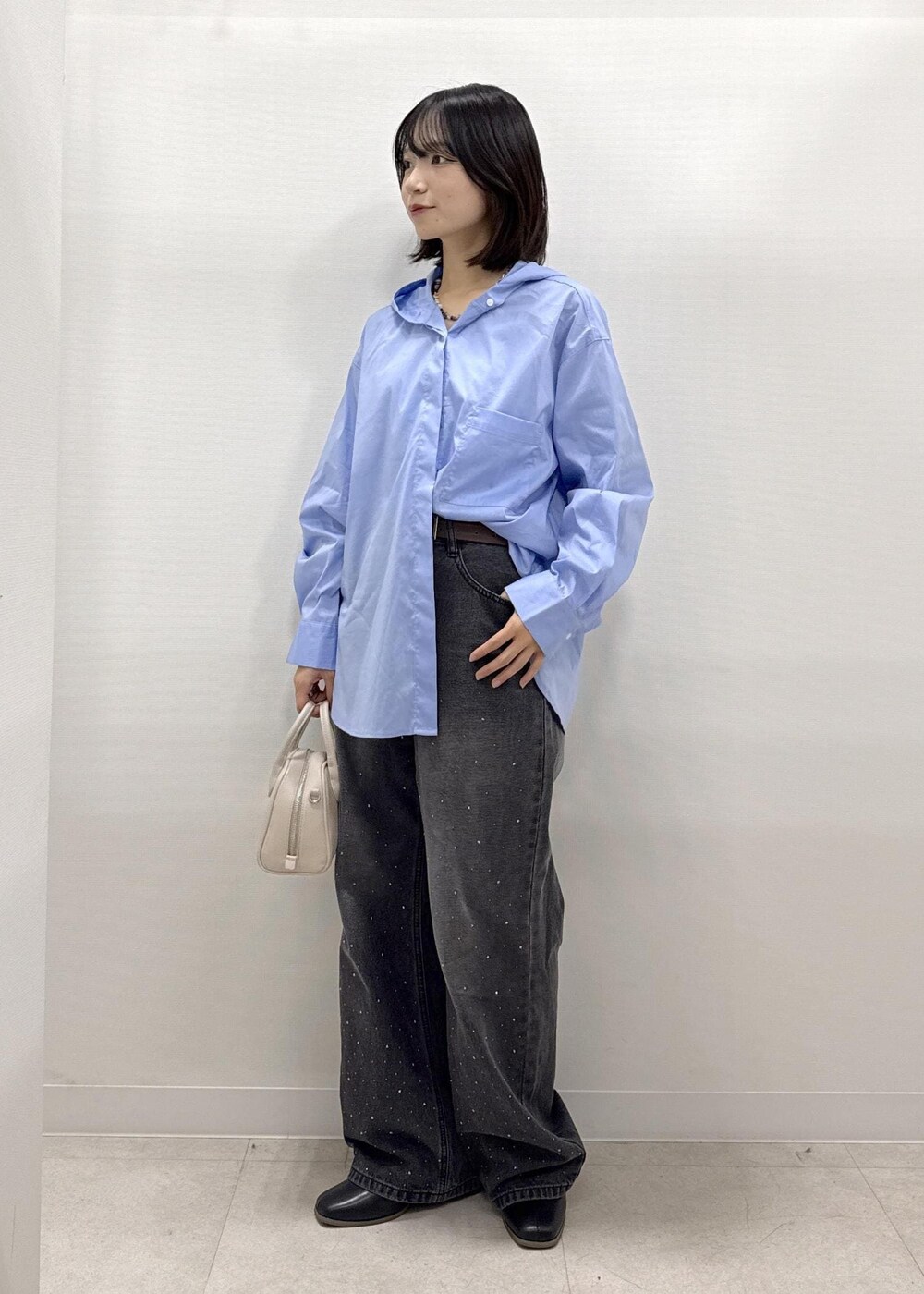 ブラック系のデニムパンツ、ブラック系のブーツ、ベージュ系のショルダーバッグを着用したレディースの秋コーディネートの2枚目の写真