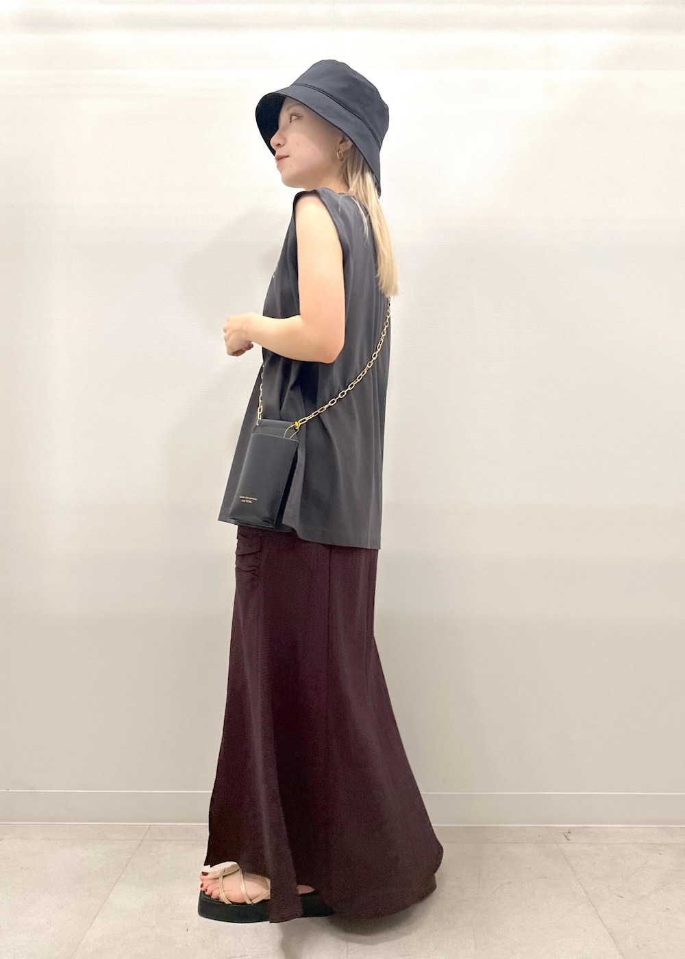 ブラック系のショルダーバッグ、ゴールド系のサンダル、グレー系のTシャツ/カットソーを着用したレディースの夏コーディネートの3枚目の写真