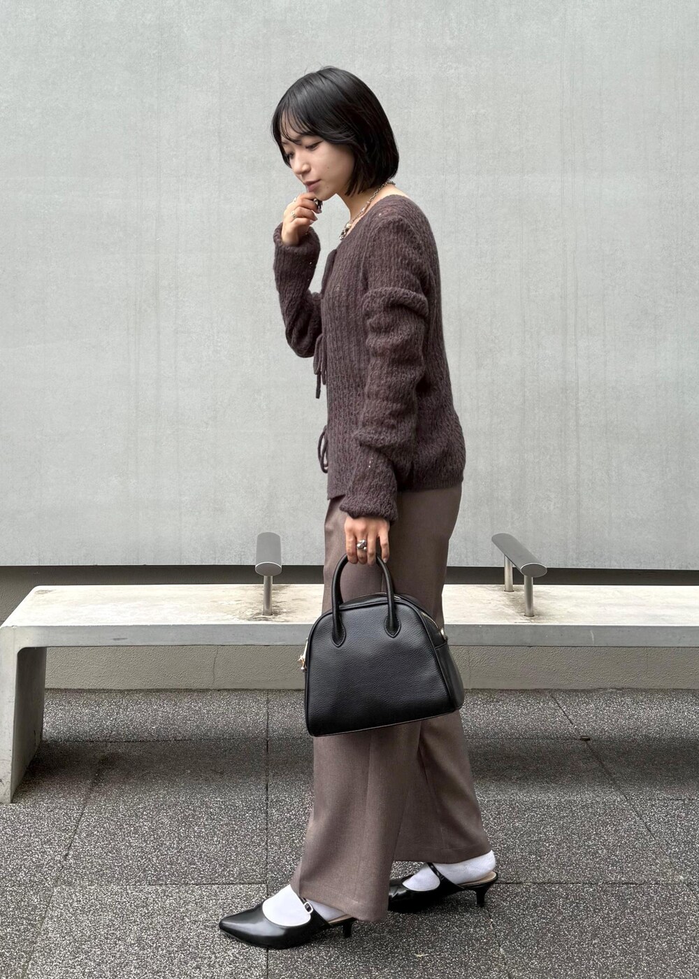 ブラウン系のカーディガン/ボレロ、ベージュ系のスラックス、ブラック系のボストンバッグを着用したレディースの秋コーディネートの3枚目の写真