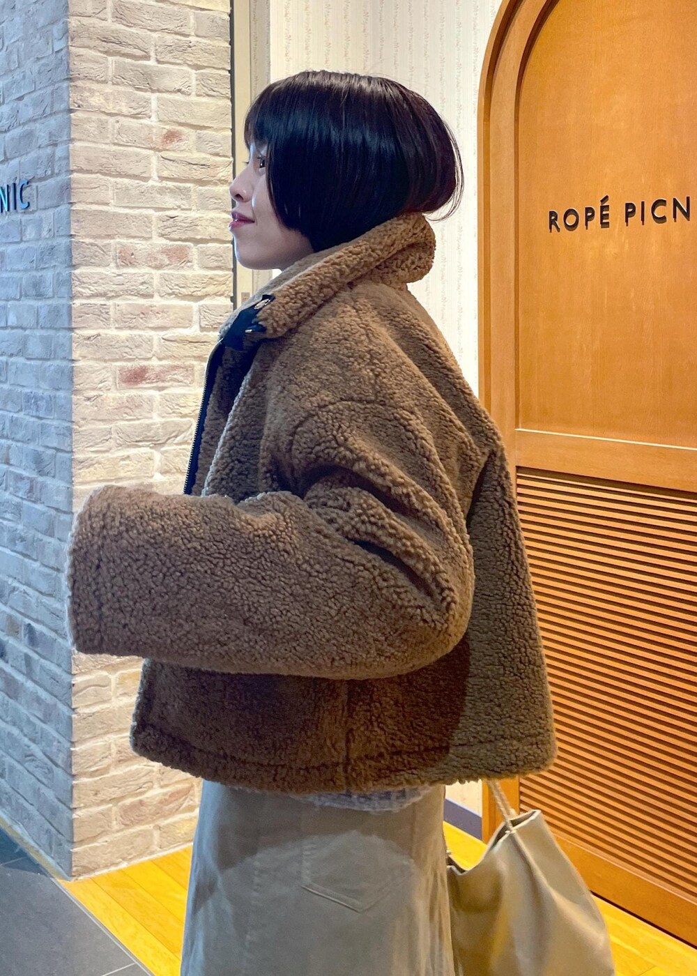 イエロー系のムートンコート、ベージュ系のスカート、ゴールド系のトートバッグを着用したレディースの冬コーディネートの7枚目の写真
