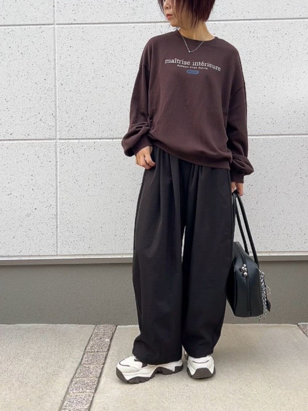 ブラウン系のスウェット、ブラック系のパンツ、ブラック系のバッグを着用したレディースの秋コーディネートの2枚目の写真